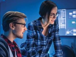 Two people look at a set of computer monitors