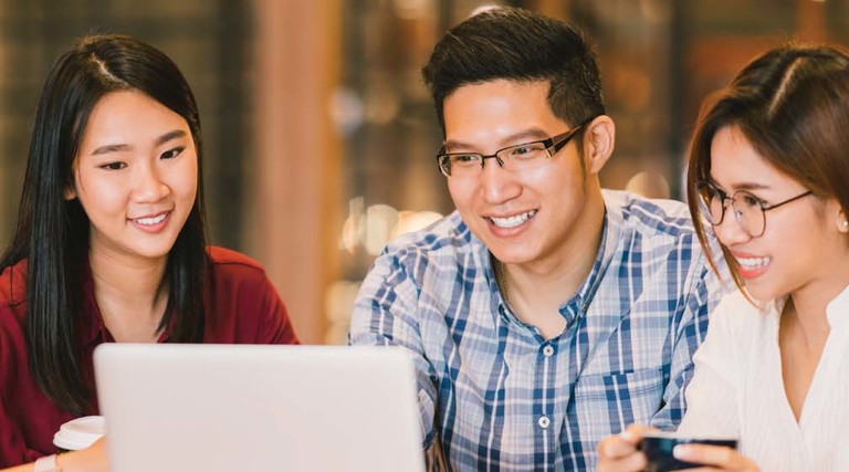 Three students look at a laptop
