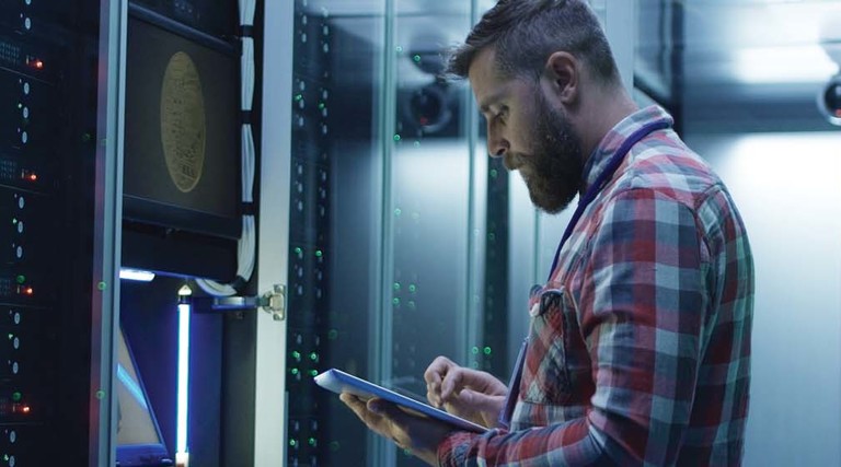 A man works on a tablet inside a large data center